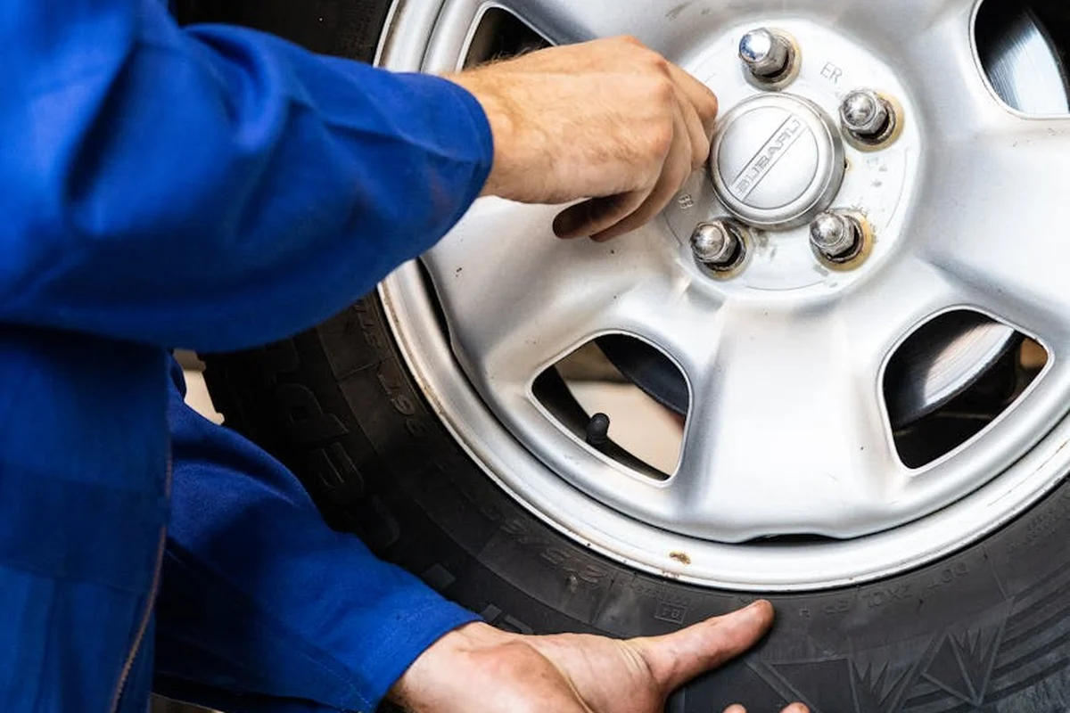 Close-up of a mechanic's hands in blue coveralls working on a car wheel.