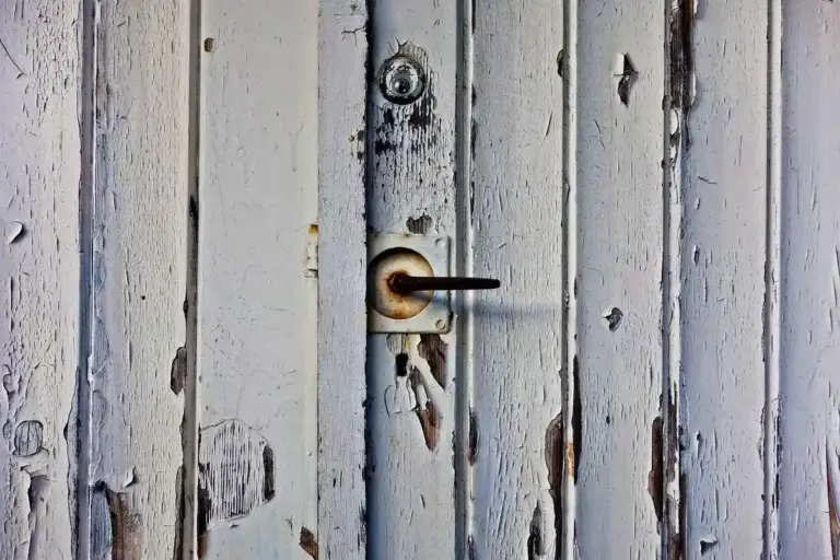 Close-up of a weathered wooden garage door with white peeling paint and a rusty handle