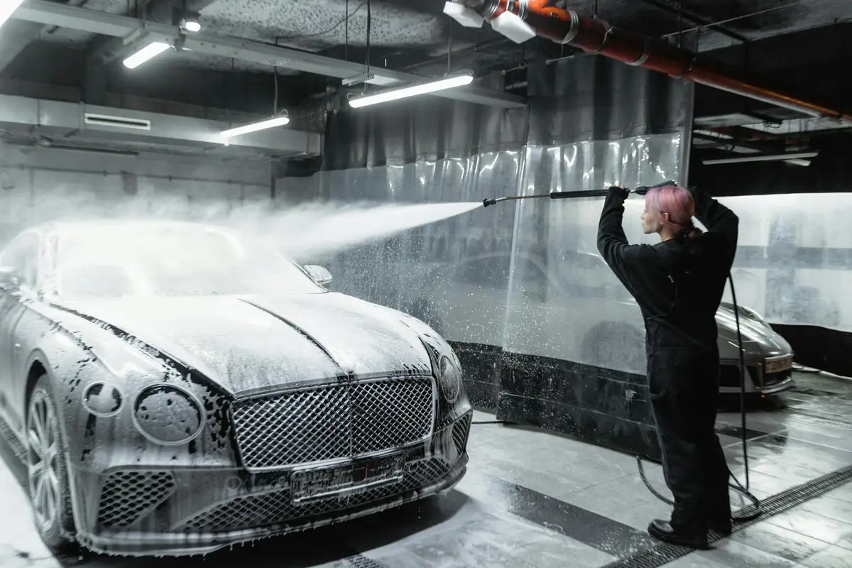 A person washing a car with a high-pressure spray in a bright, modern garage wash bay.