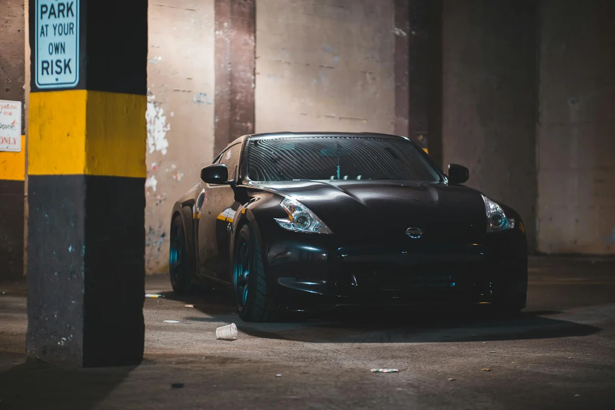 Dark sports car parked in a dimly lit concrete parking garage with a yellow-striped pillar.