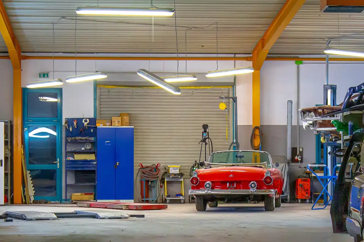 A tidy garage workshop featuring a red vintage convertible car, blue tool cabinets, and various equipment, illustrating a typical space where moisture control and temperature solutions are evaluated.