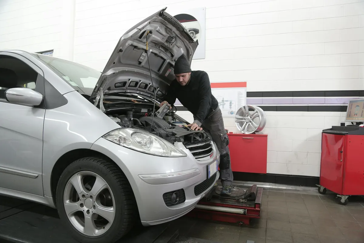 Mechanic working on a car with the hood open in a bright garage workshop.