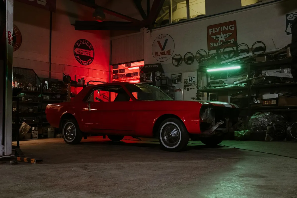 Red vintage car inside a cluttered repair shop with neon lighting and various signs on the walls.