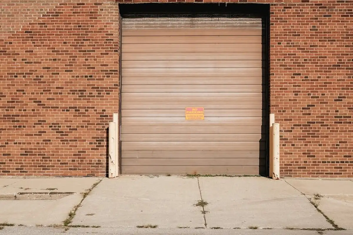 Closed beige roll-up garage door in a brick building with a concrete driveway.