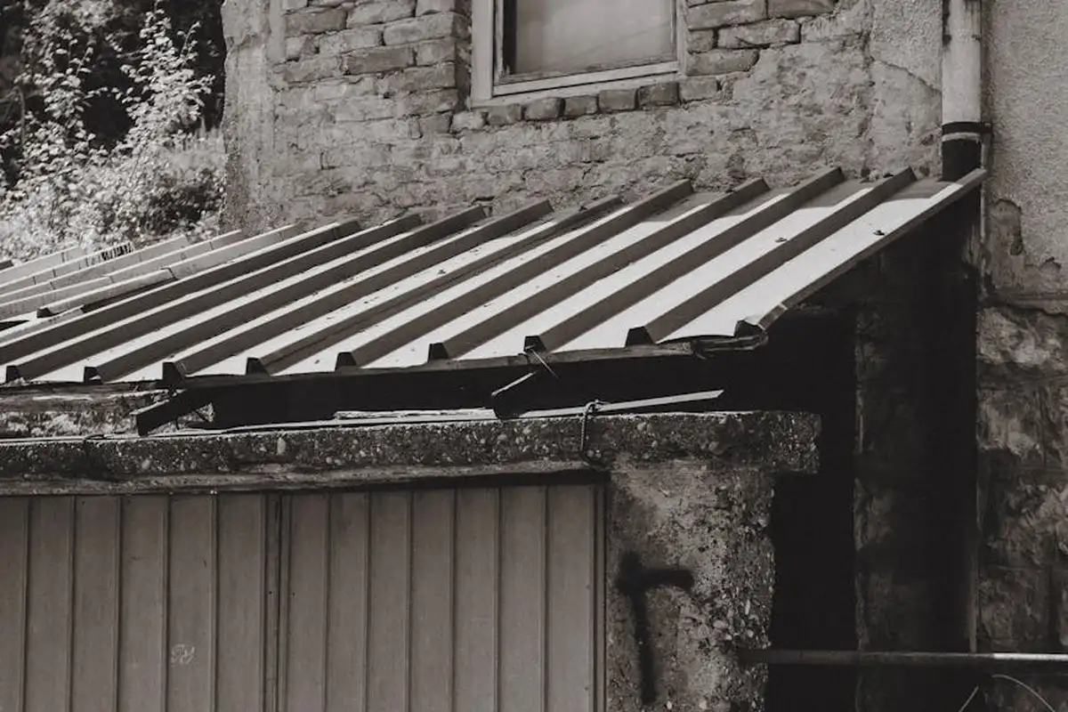 Black-and-white photo of a small garage with a corrugated metal roof and a vertical-panel garage door.