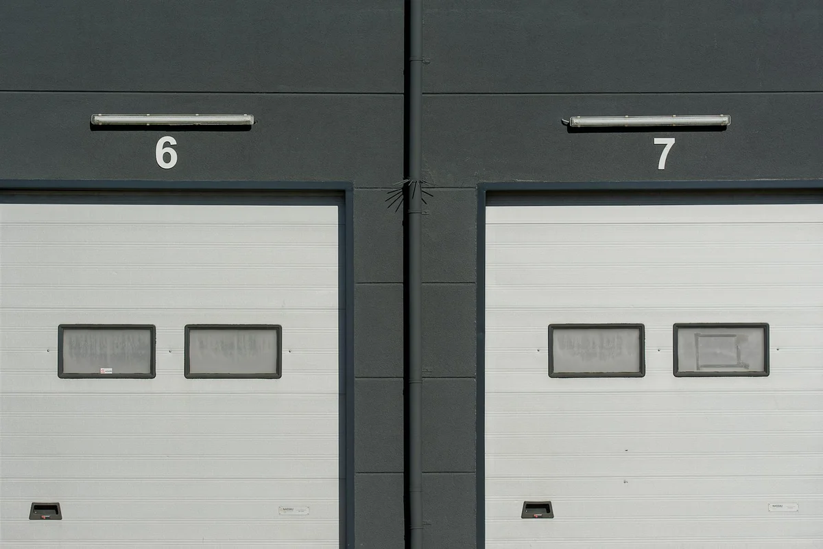 Two gray garage doors labeled '6' and '7' on a dark exterior wall.