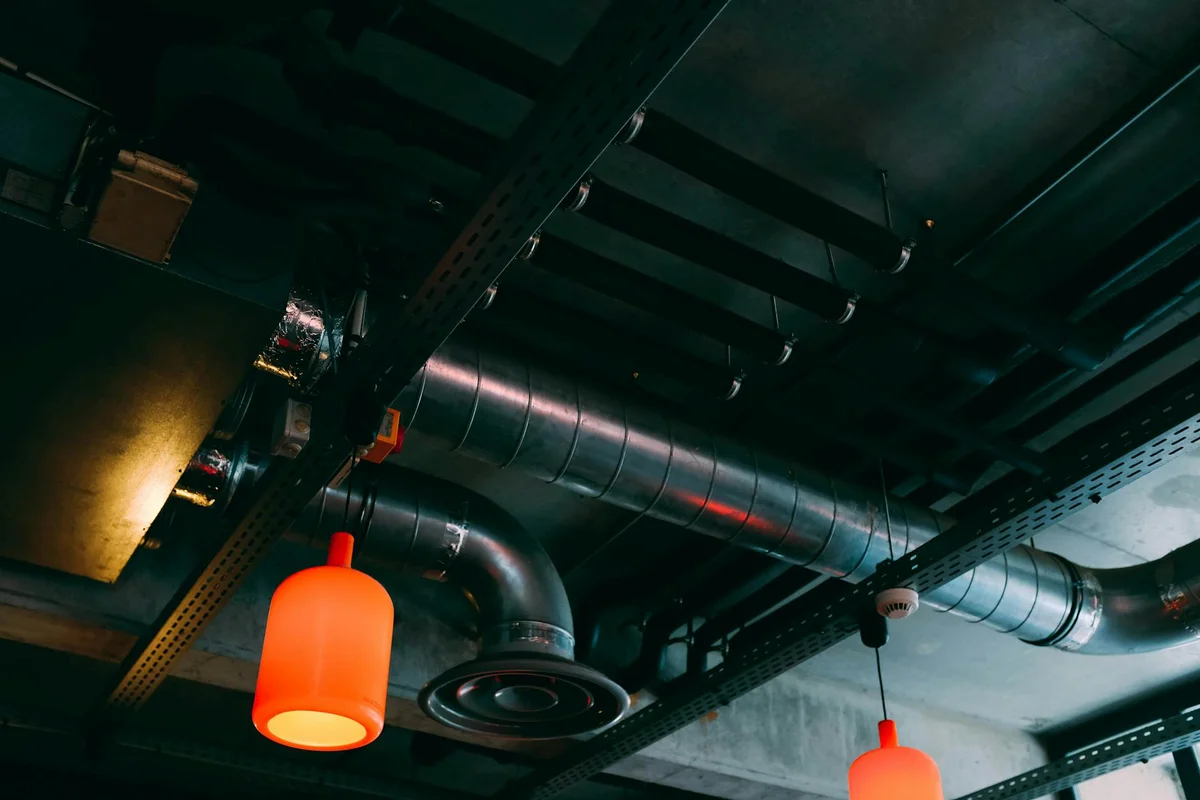 Garage ceiling with exposed ducts and circular vent fittings, illuminated by orange pendant lights