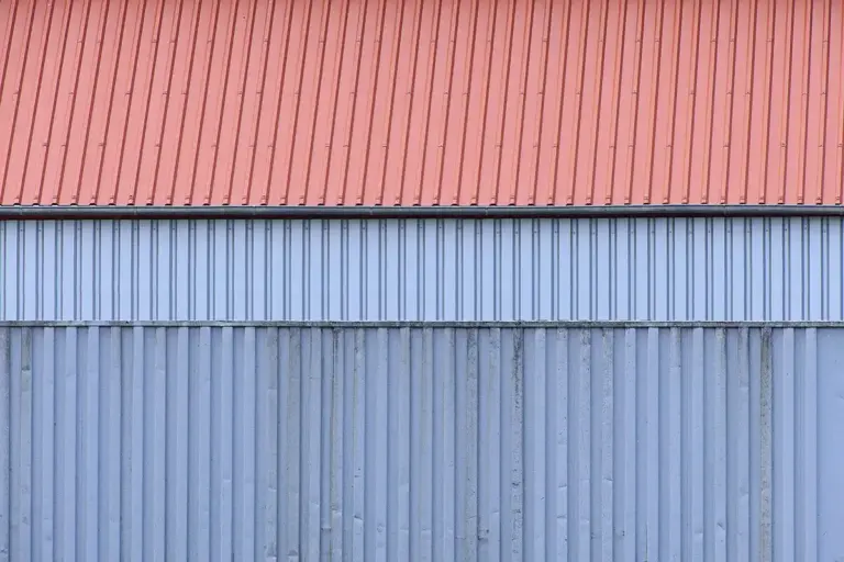 Close-up of corrugated metal panels on a garage, with red panels on the upper section and blue panels on the lower section.