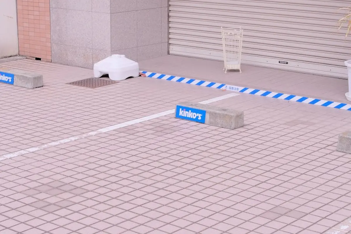 An outdoor scene showing a closed garage door with blue-and-white caution tape, barriers, and blocks in front, illustrating that safety features are not universal across all garage door openers.