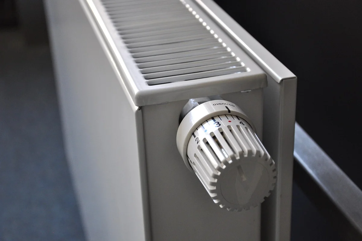 Close-up of a white radiator thermostat knob on a metal heater in a garage.