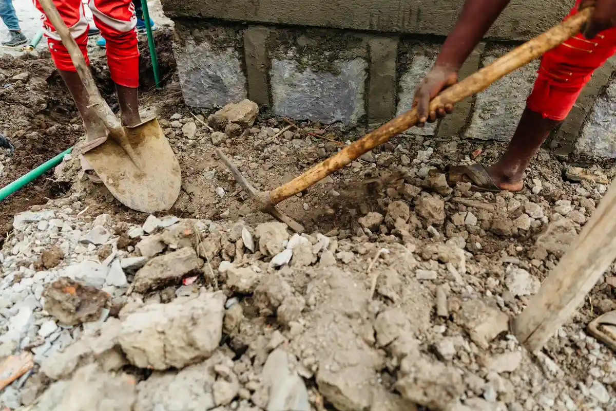 Construction site on a rocky, sloped yard with workers shoveling soil near a concrete foundation