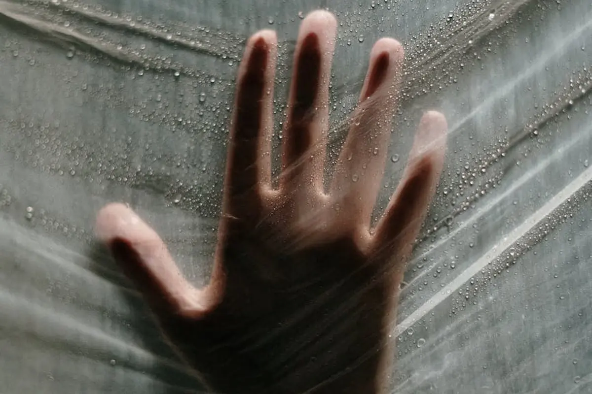Bare hand pressed against a clear plastic moisture barrier with droplets.