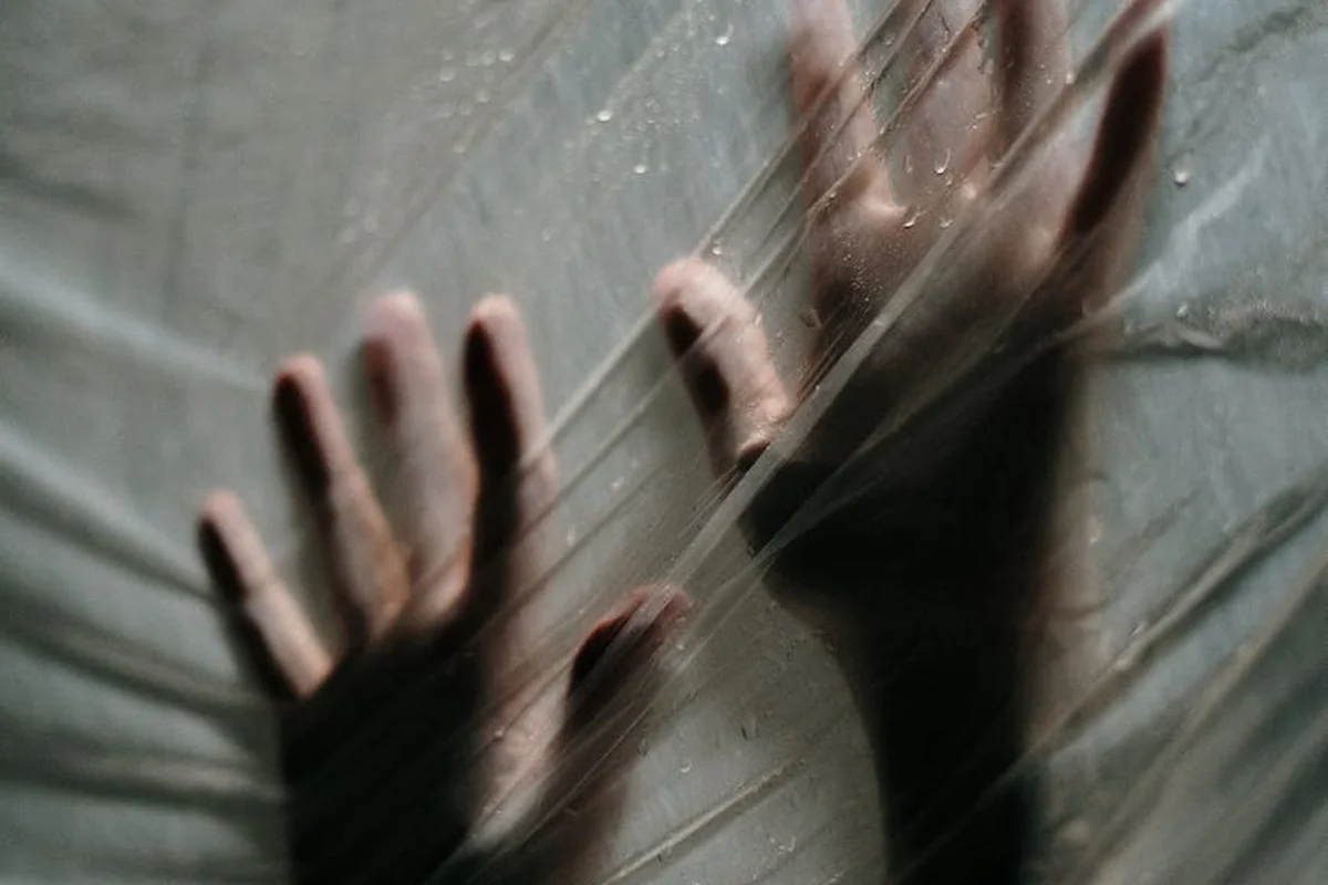 Hands pressed against a translucent plastic vapor barrier, illustrating improper sealing and potential moisture buildup in walls.