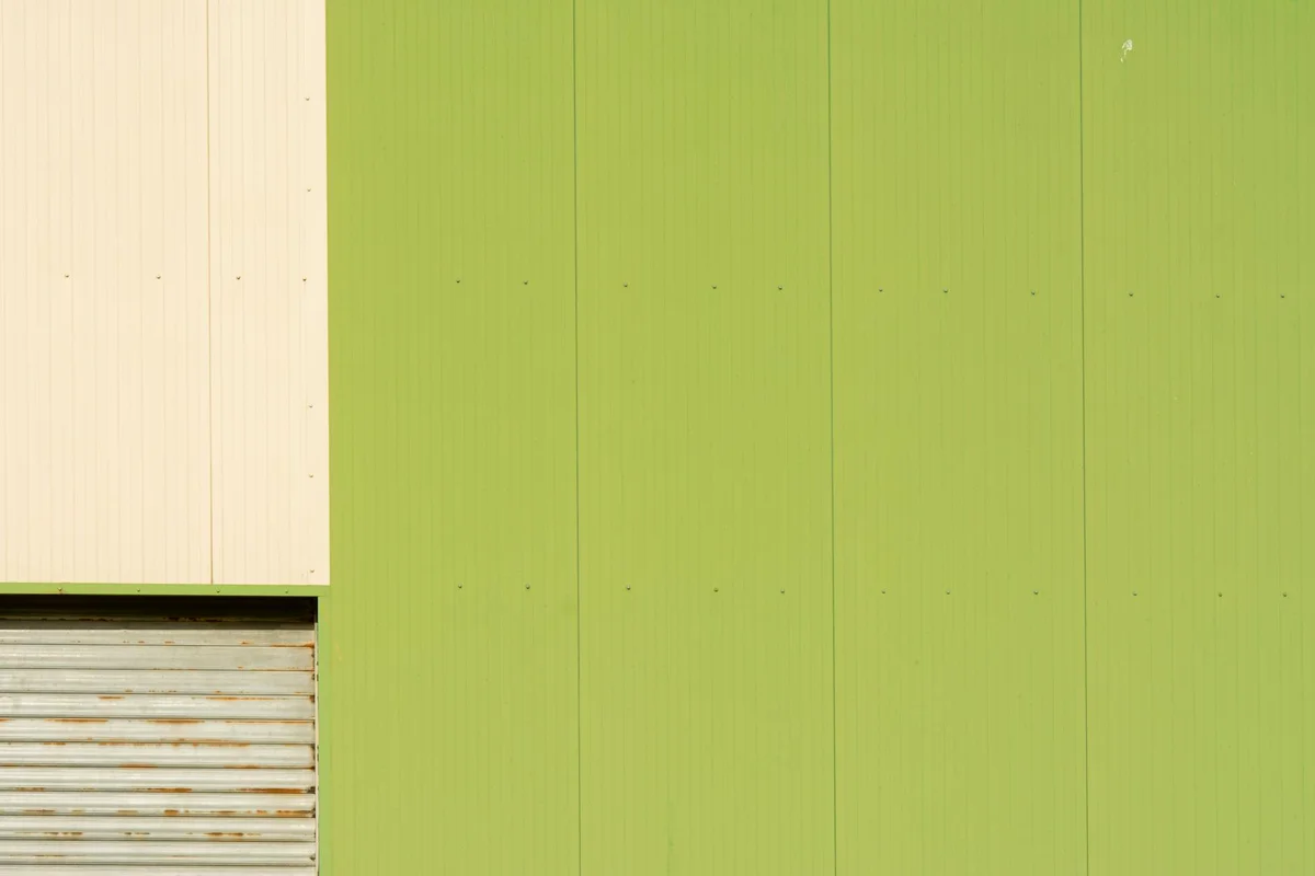 Green vertical siding wall with a beige rolling shutter partially visible on the left.
