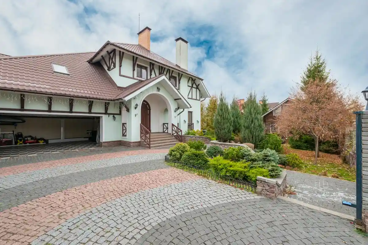 European-style house with an attached garage and a curved, cobblestone driveway, surrounded by a landscaped yard