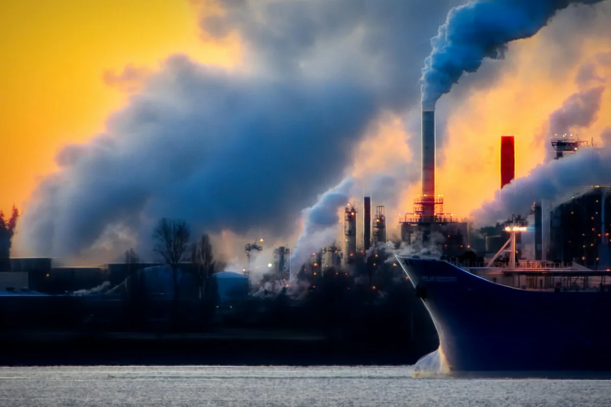 Industrial harbor scene with smokestacks emitting thick smoke over the water, illustrating air pollution