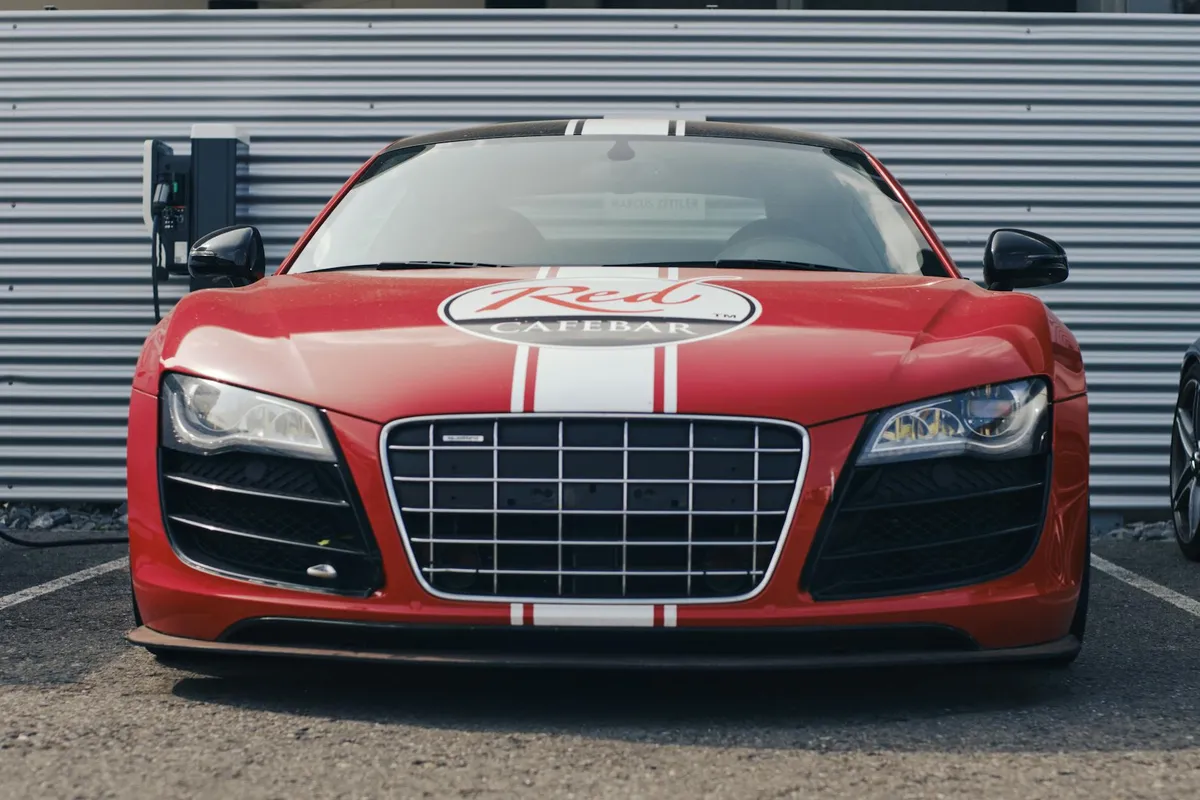Front view of a red Audi R8 with white racing stripes parked in a garage