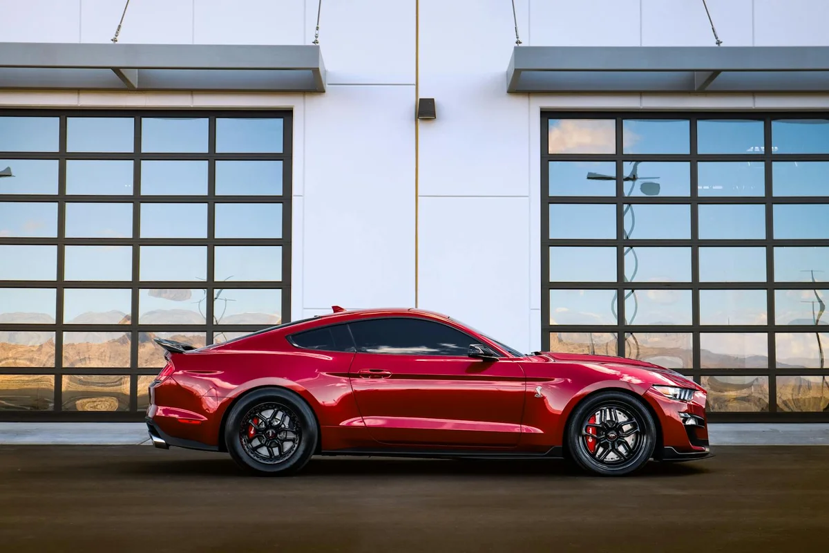 Red sports car parked beside a modern glass-panel garage door.