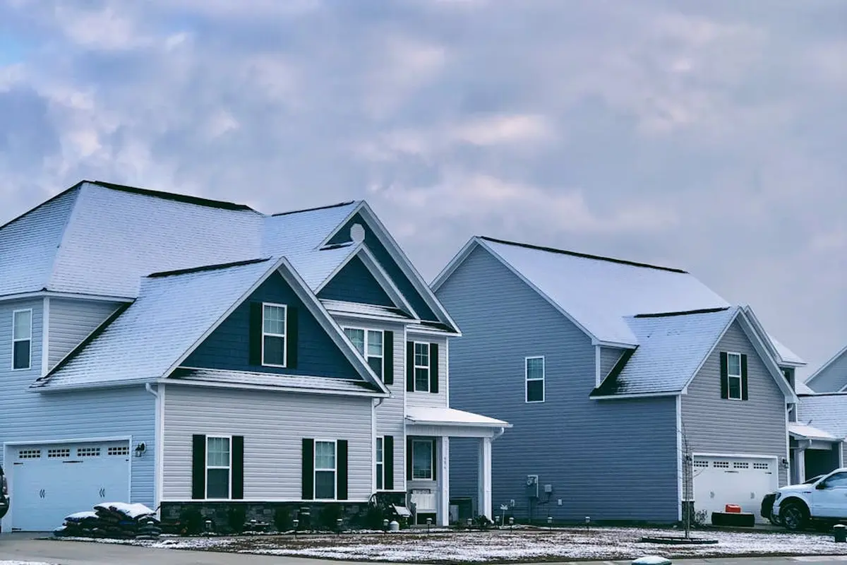 Row of snow-dusted suburban houses with attached garages in a residential neighborhood.