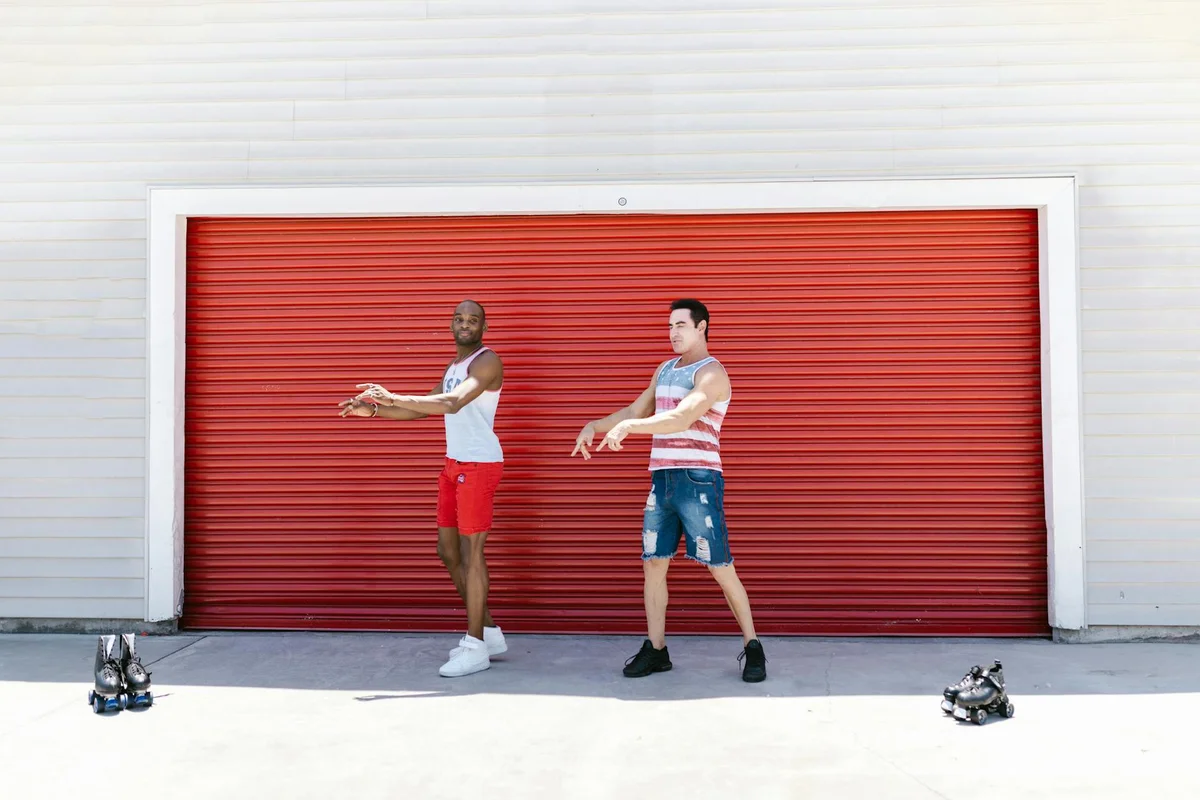Two men standing in front of a red garage door, stretching their arms.